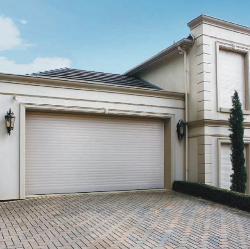 Beige garage door on a light stucco house with brick driveway and blue sky.