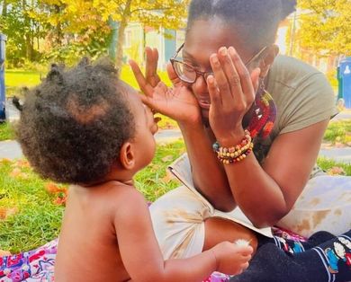 Image of Our Mommie Village Doula Shyana playing peekaboo with a baby at an Our Mommie Village meetup