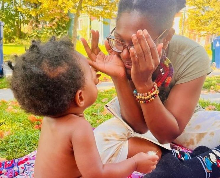 Image of Our Mommie Village doula Shyana at an Our Mommie Village meetup playing peekaboo with a baby