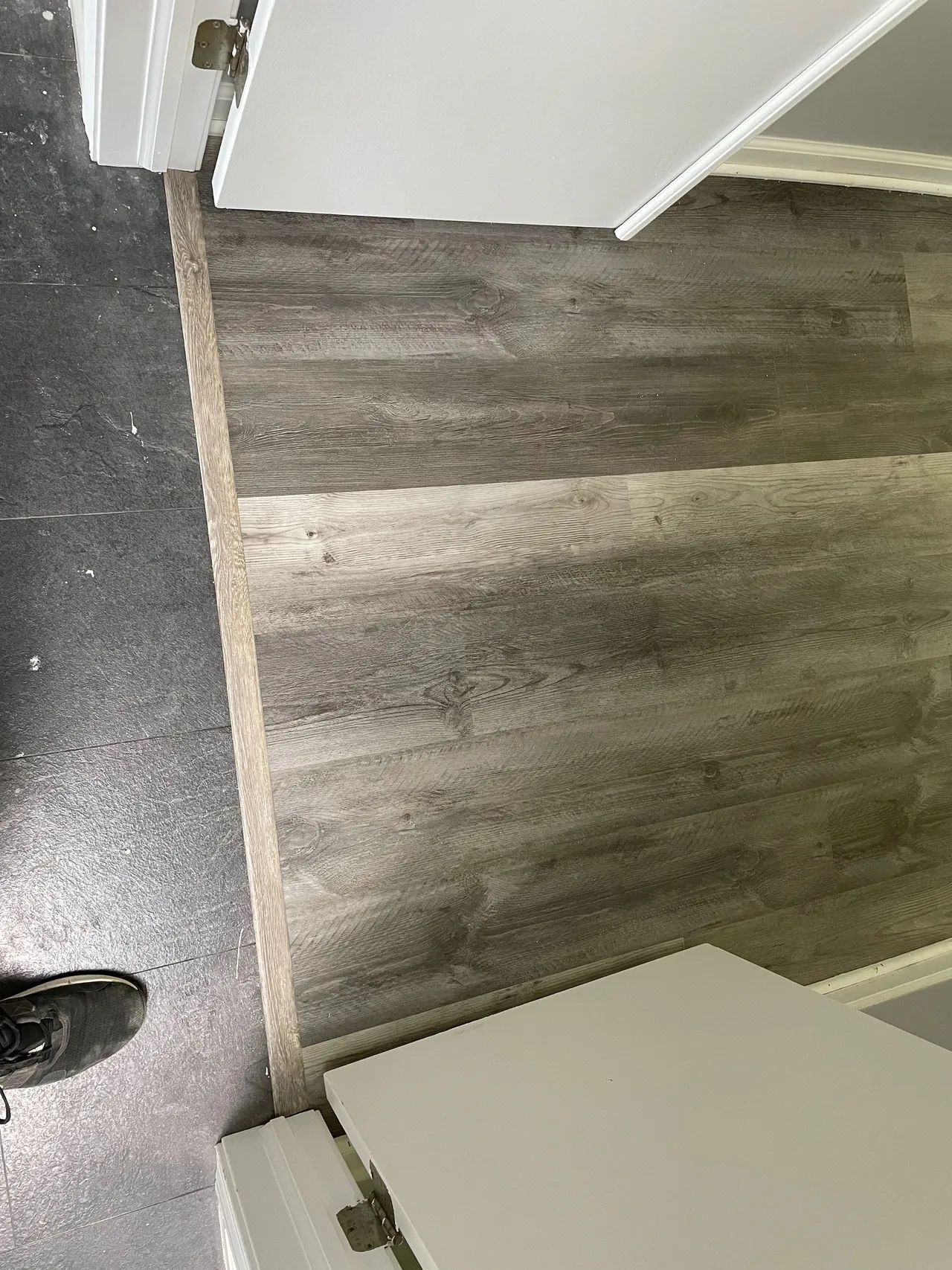 A person is standing on a wooden floor next to a door.
