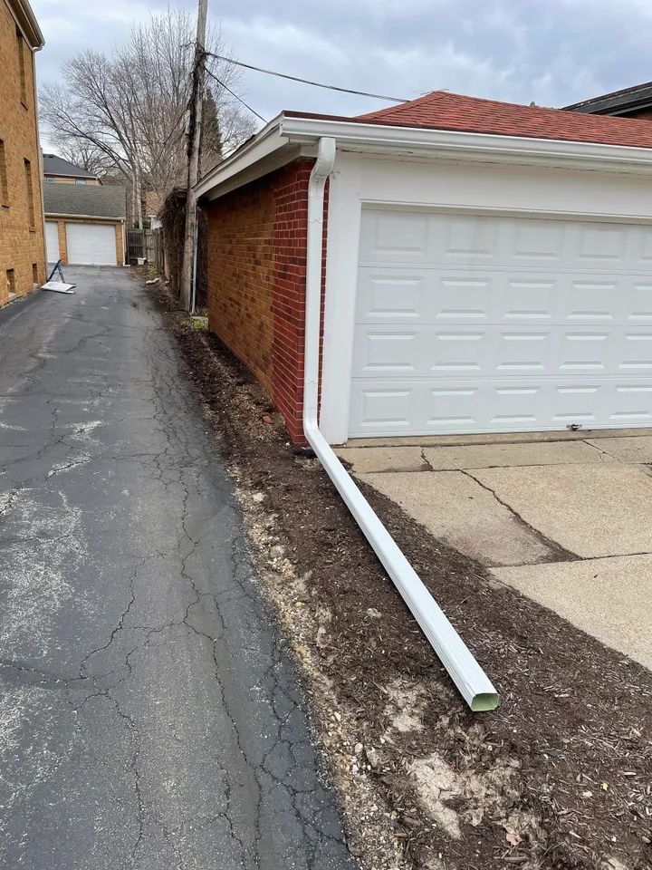 White gutter downspout extending from garage. Professional gutter installation service and siding and gutter repair.