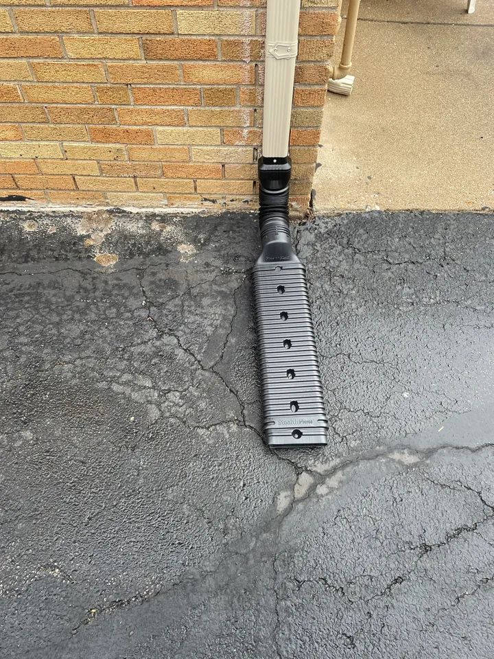 Black gutter downspout extension on driveway. Reliable handyman for gutter repair and gutter installation service.