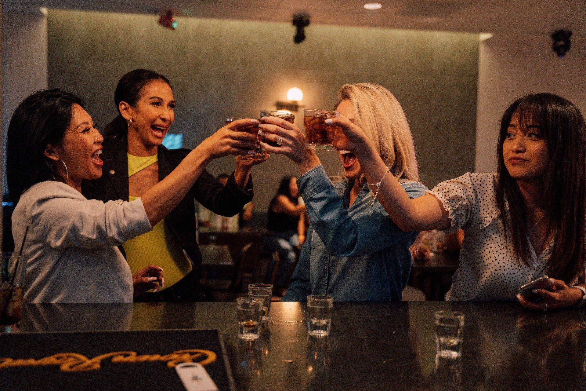 A group of lady friends toasting their cocktails.  All of them are laughing and smiling.