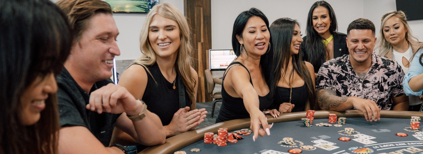 A group of young friends gather around a blackjack table and are all smiling and laughing while …