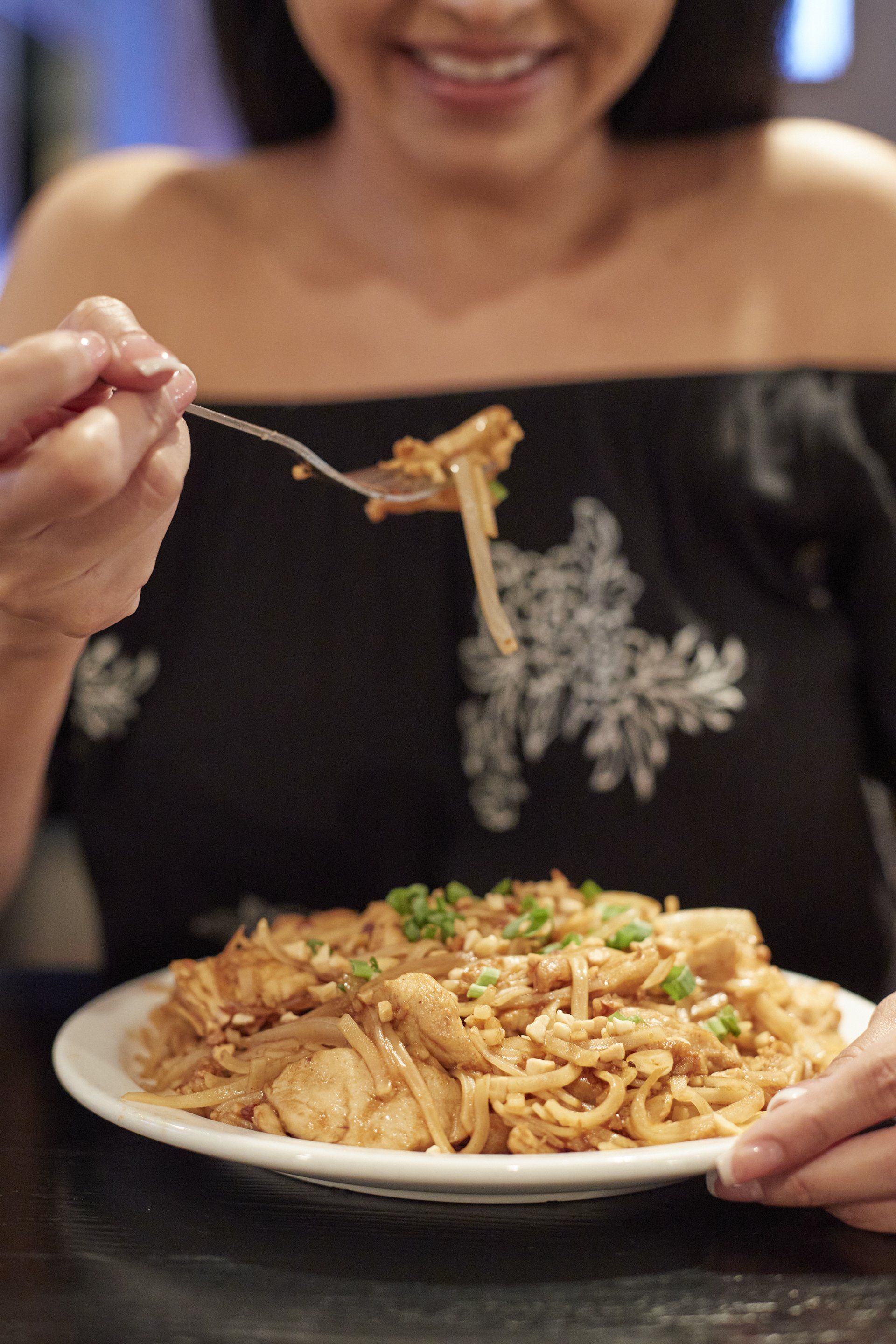 A woman begins eating the delicious noodles that were cooked over a wok and flame.