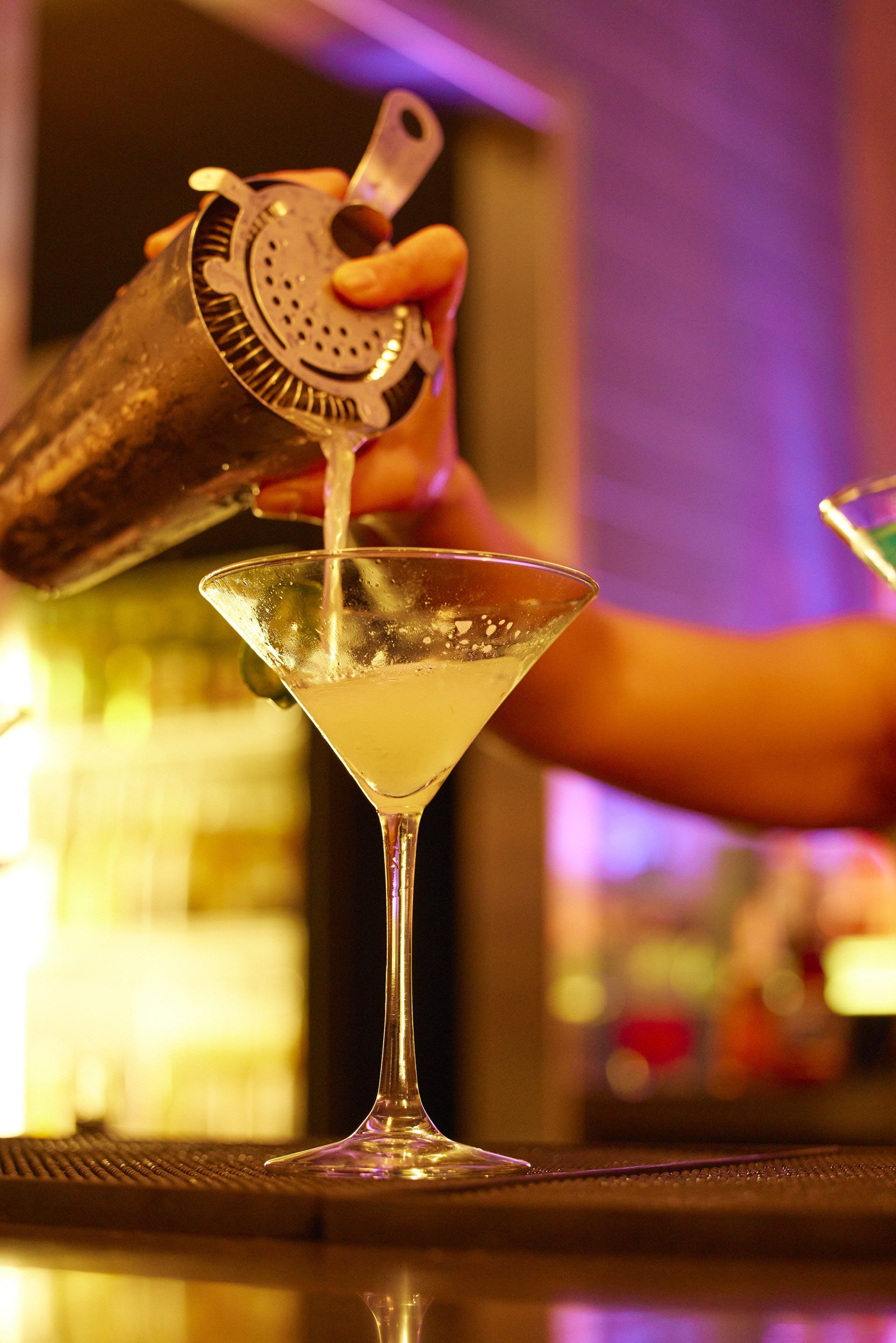 Martini being made with the drink being poured into the martini glass.