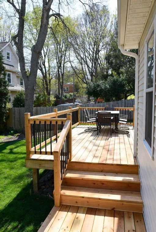 Wooden deck with steps, railings, and outdoor dining area. Green grass and trees in background.