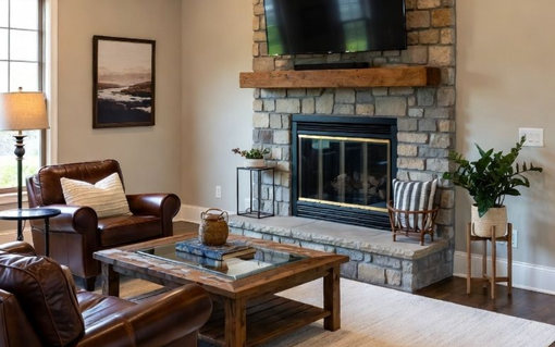 Living room with stone fireplace, brown leather chairs, wooden coffee table, and large window.