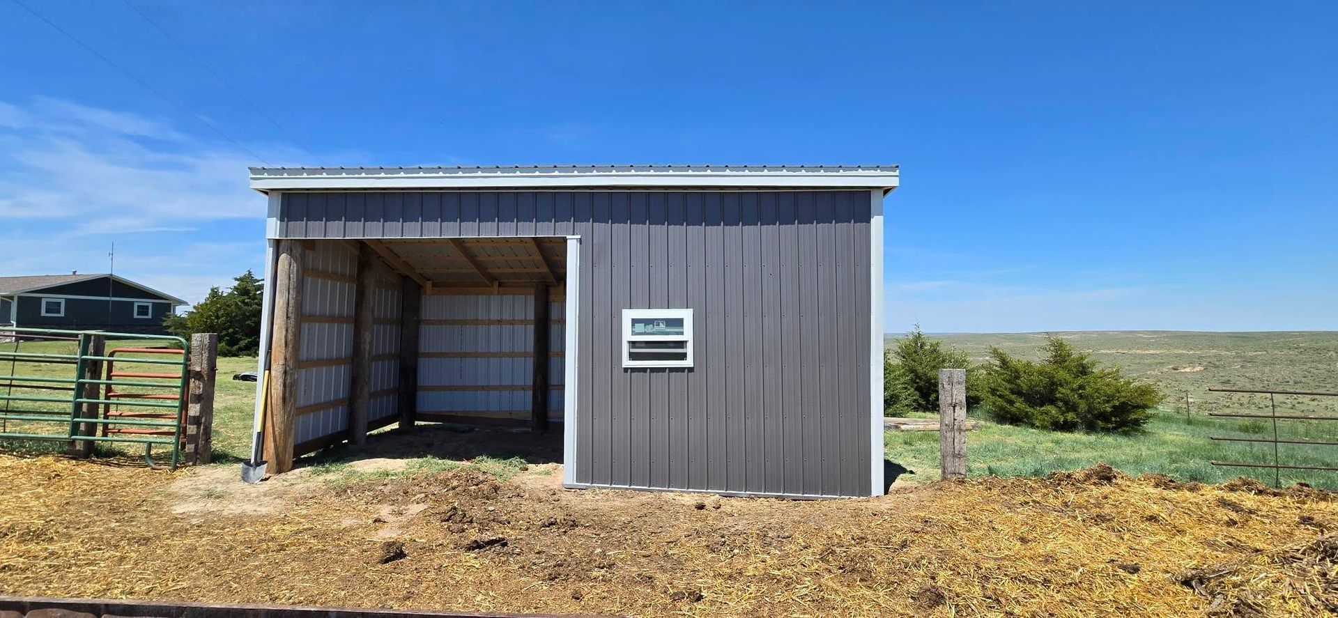 A gray shed with an open side, small window, and a blue sky in the background.