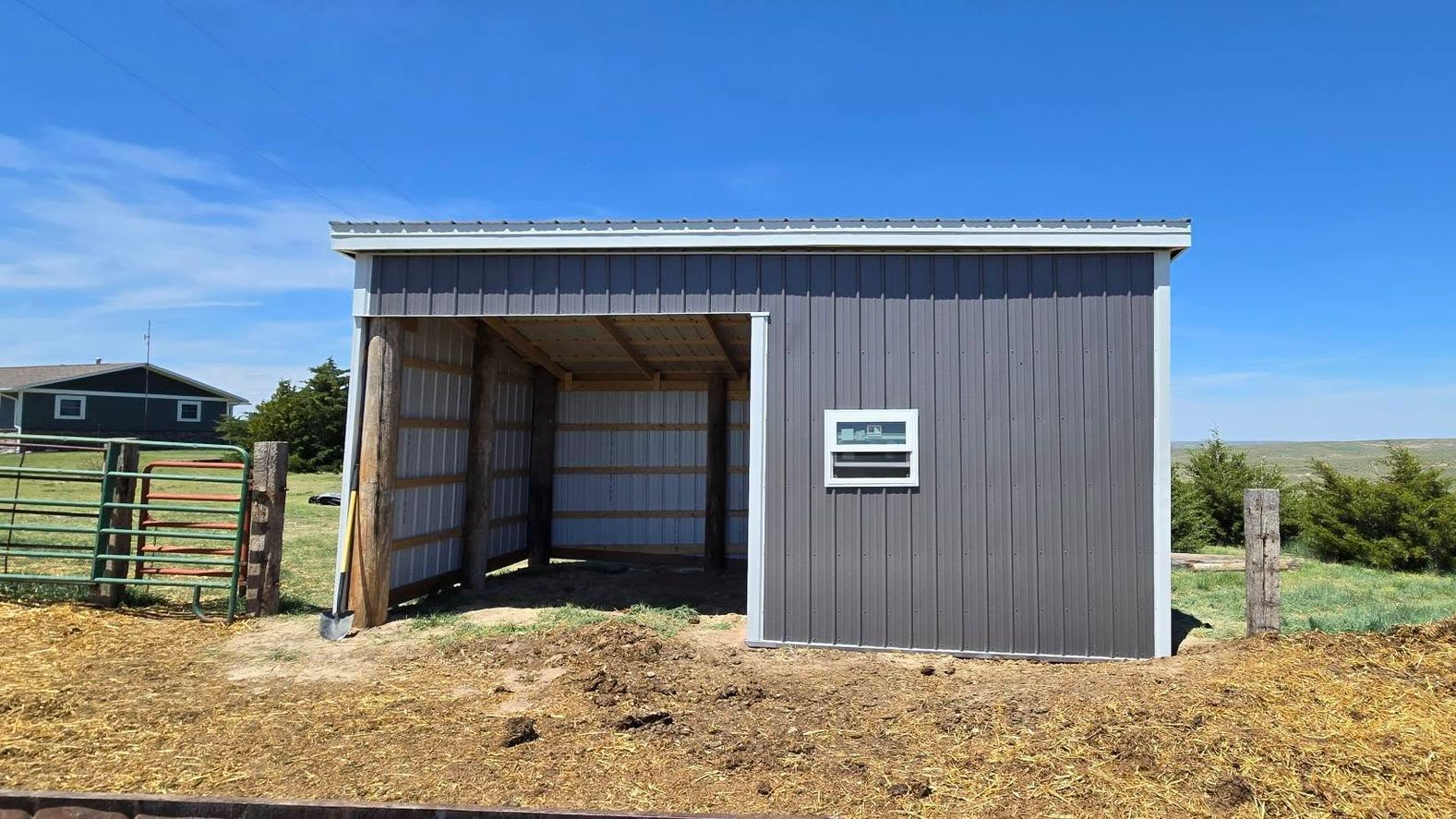 Gray shed with open front, small window, and metal roof, set against a blue sky.
