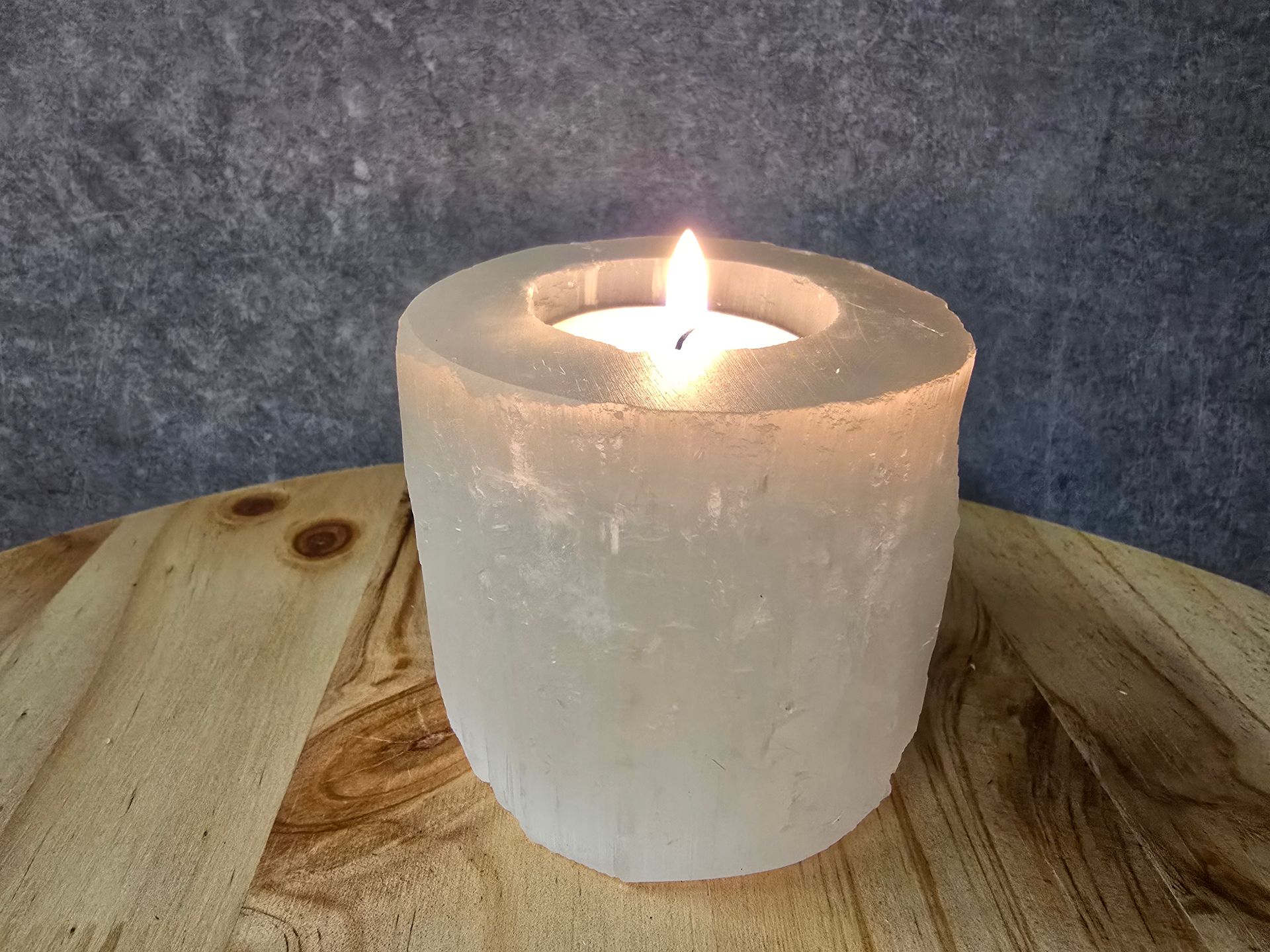 Een kaars brandt in een kaarsenhouder op een houten tafel.