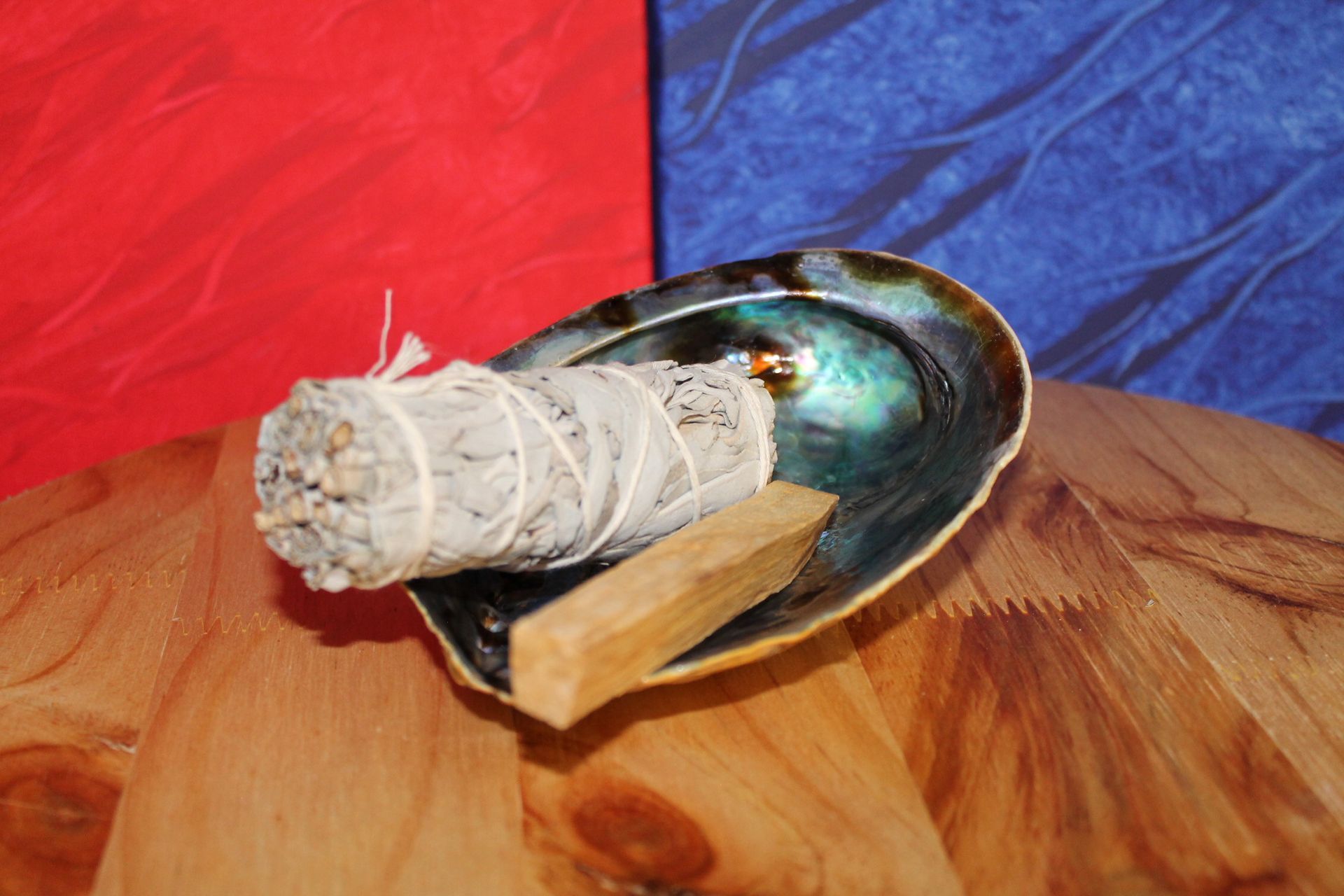 Een witte saliestok en een palo santostok liggen in een schelp op een houten tafel.