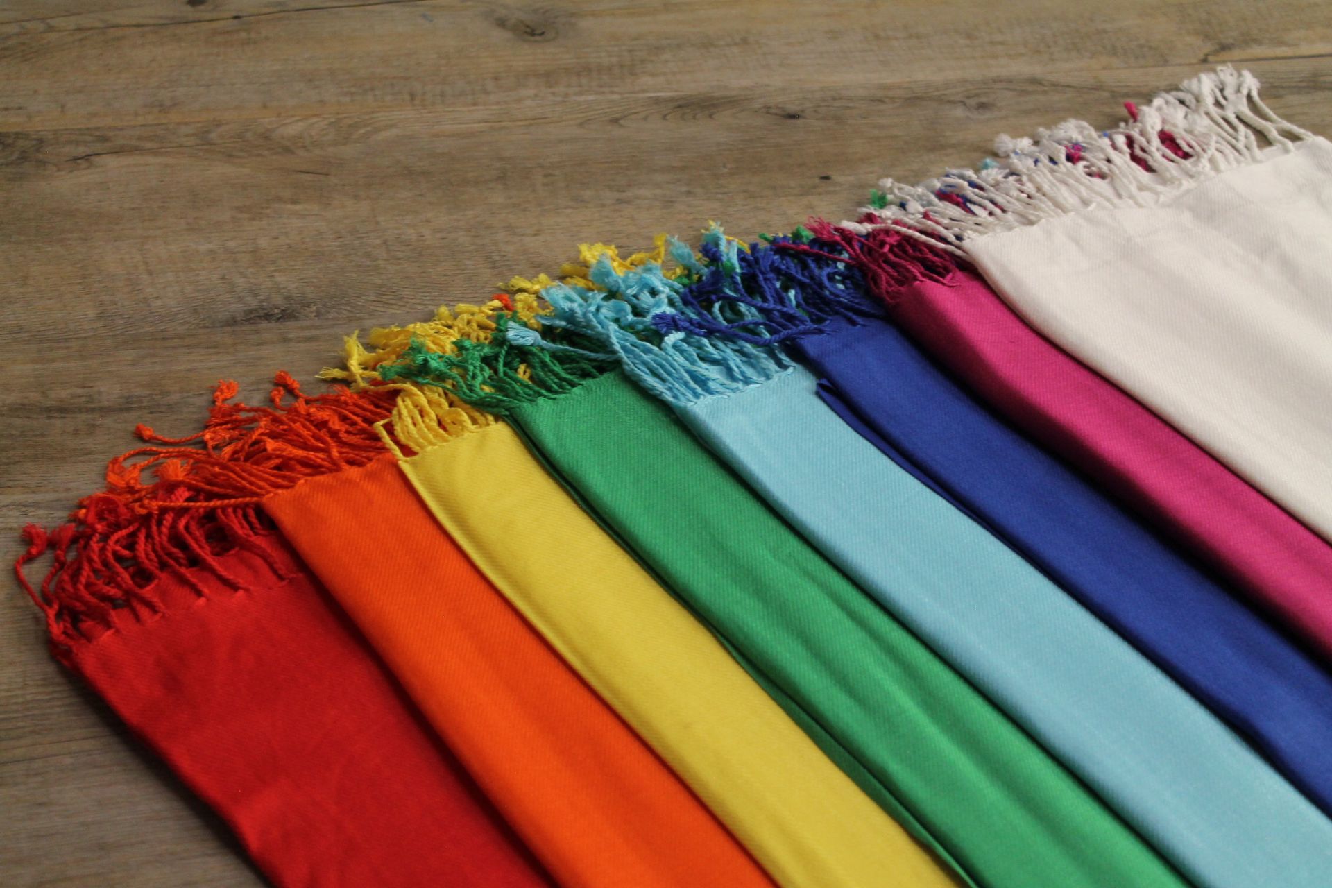 Een rij kleurrijke sjaals ligt op een houten tafel.