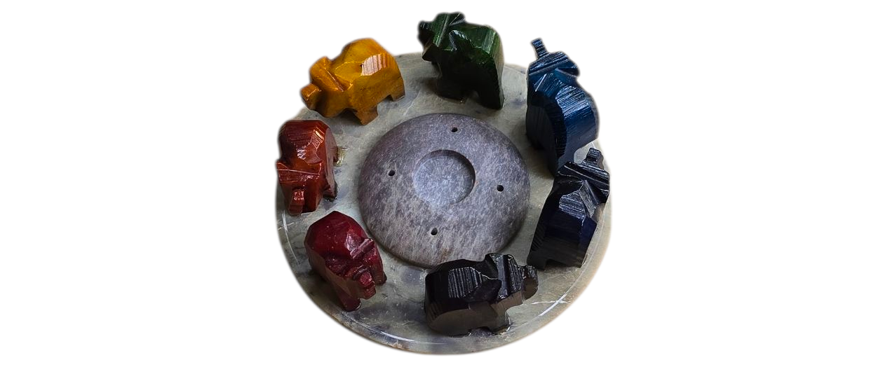 Een ronde stenen sokkel met acht kleine, kleurrijke olifantenbeeldjes rond een centrale grijze steen.