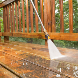 A person is using a high pressure washer to clean a wooden deck.