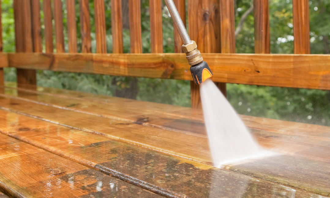 A person is using a high pressure washer to clean a wooden deck.