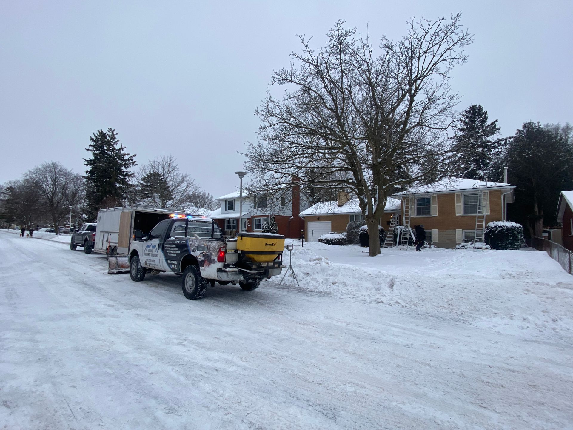 A truck is driving down a snowy street next to a house