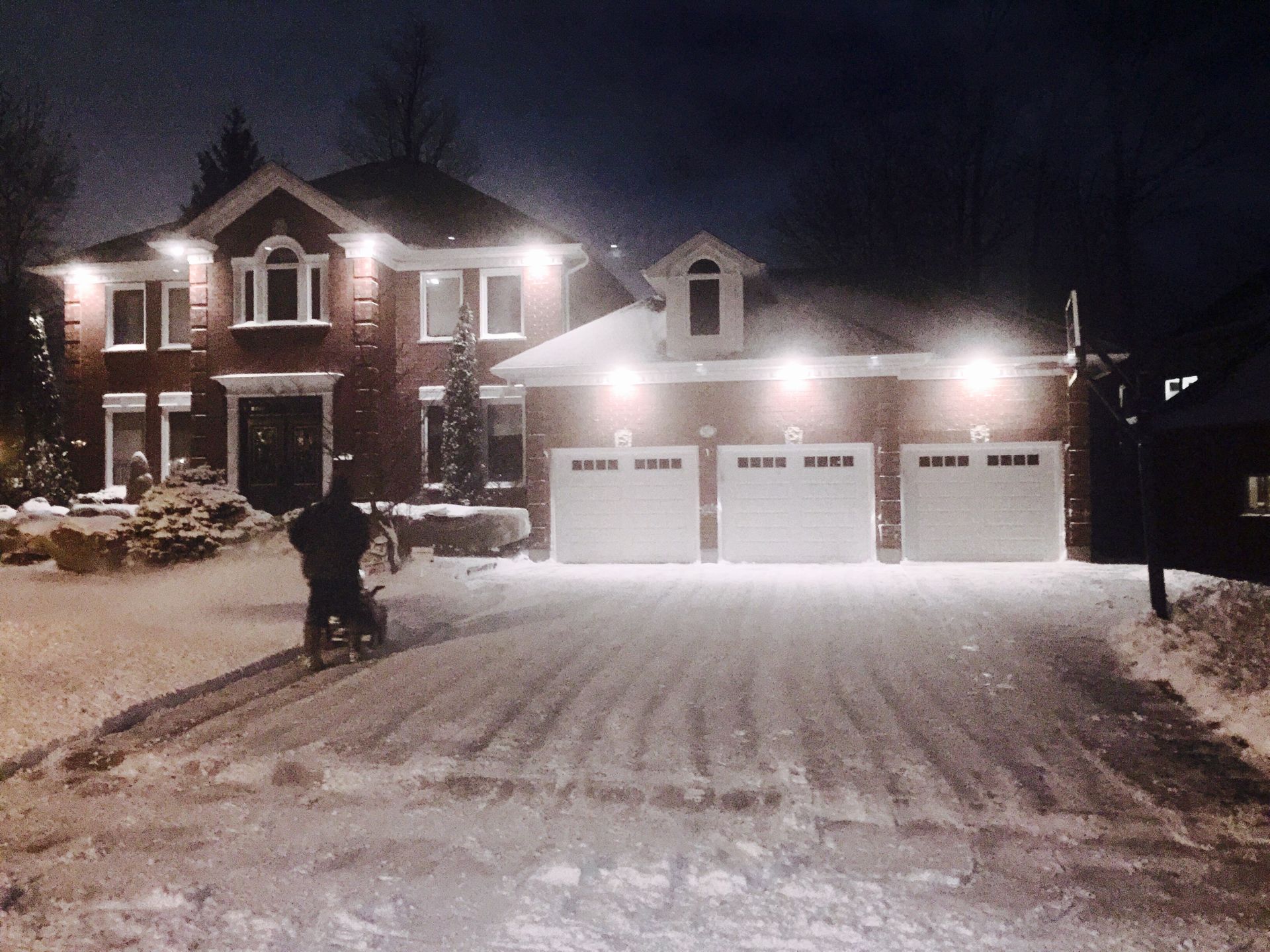 A man is shoveling snow in front of a house at night