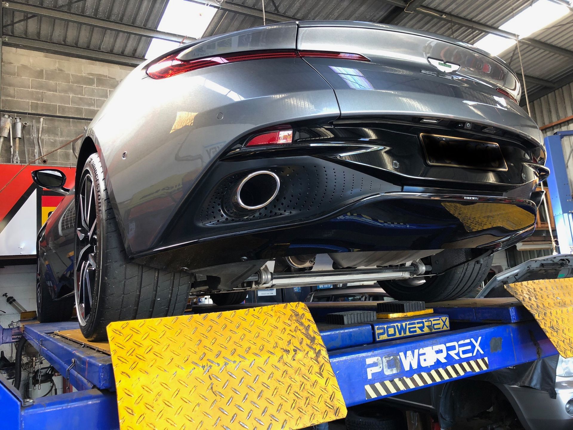 Gray Aston Martin sports car on a hydraulic lift in a repair shop.— One Stop Service and Suspension Centre In Port Macquarie, NSW