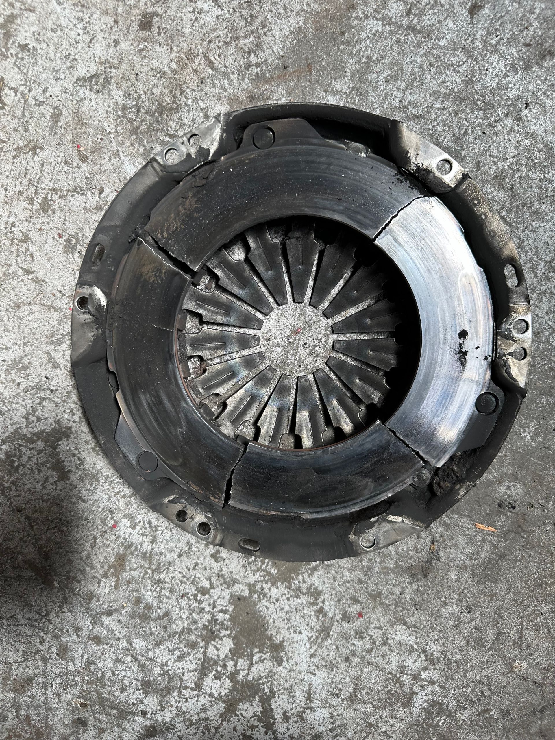 Damaged clutch plate on a gray surface, with cracks in the friction material and wear.— One Stop Service and Suspension Centre In Port Macquarie, NSW
