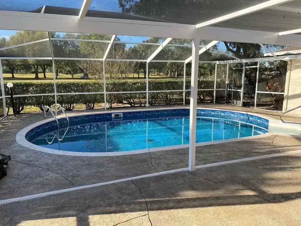 A large swimming pool is surrounded by a screened in area.