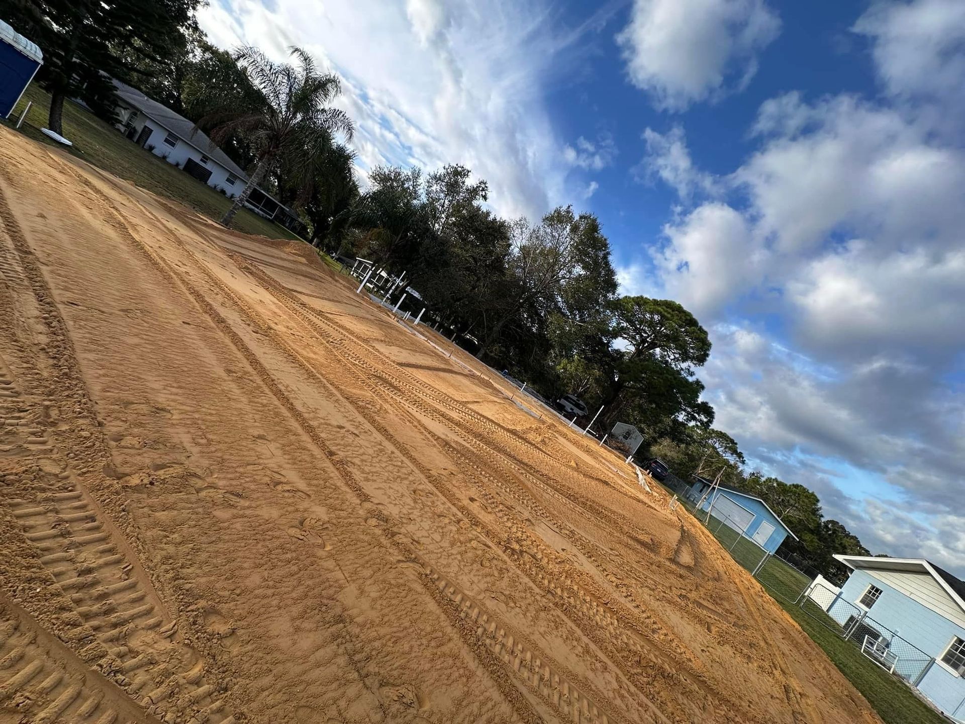 A dirt field with a blue building in the background and trees in the background.