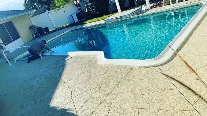 A man is working on the side of a swimming pool.