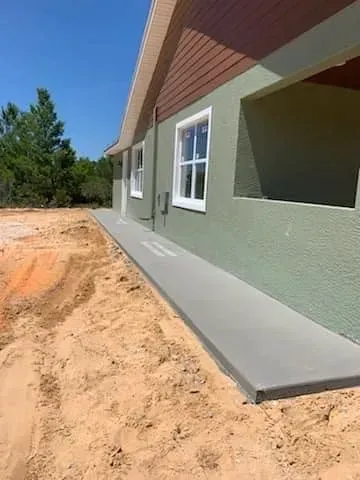 A concrete walkway is being built on the side of a house.