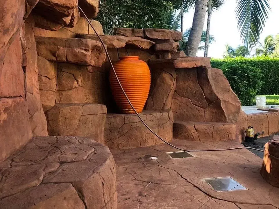 A large orange vase is sitting in front of a rock wall.