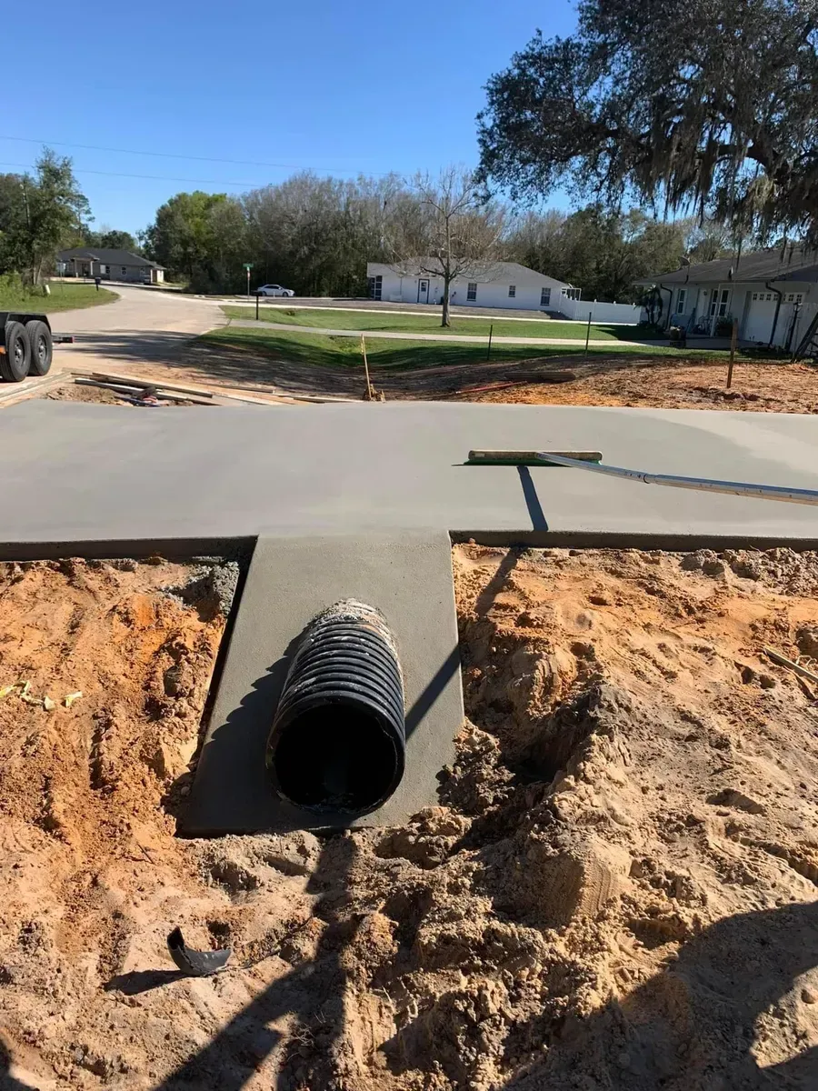 A black pipe is sitting in the dirt next to a concrete curb.