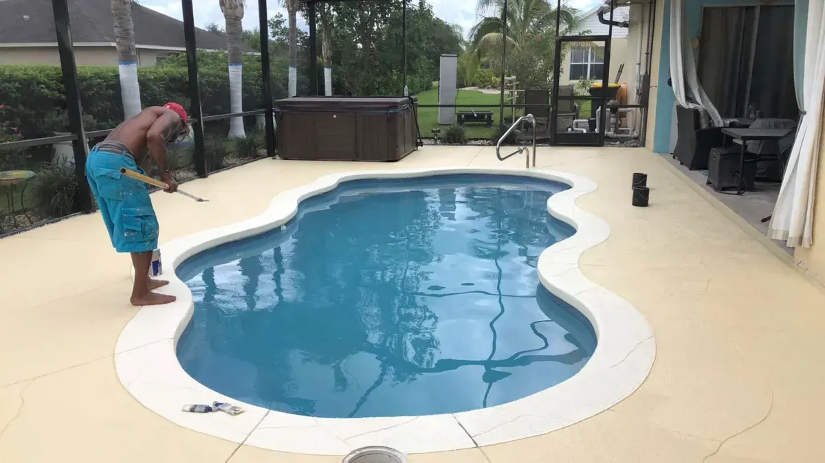 A man is cleaning a swimming pool with a broom.