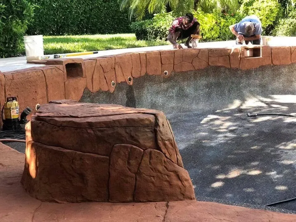 Two men are working on the side of a swimming pool.