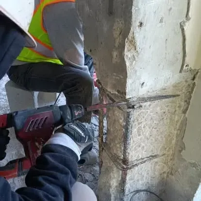 A man is using a drill to cut a hole in a concrete column.