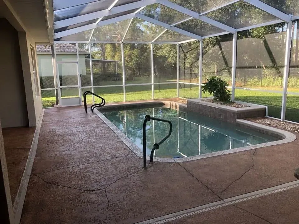 A large swimming pool is surrounded by a screened in area.