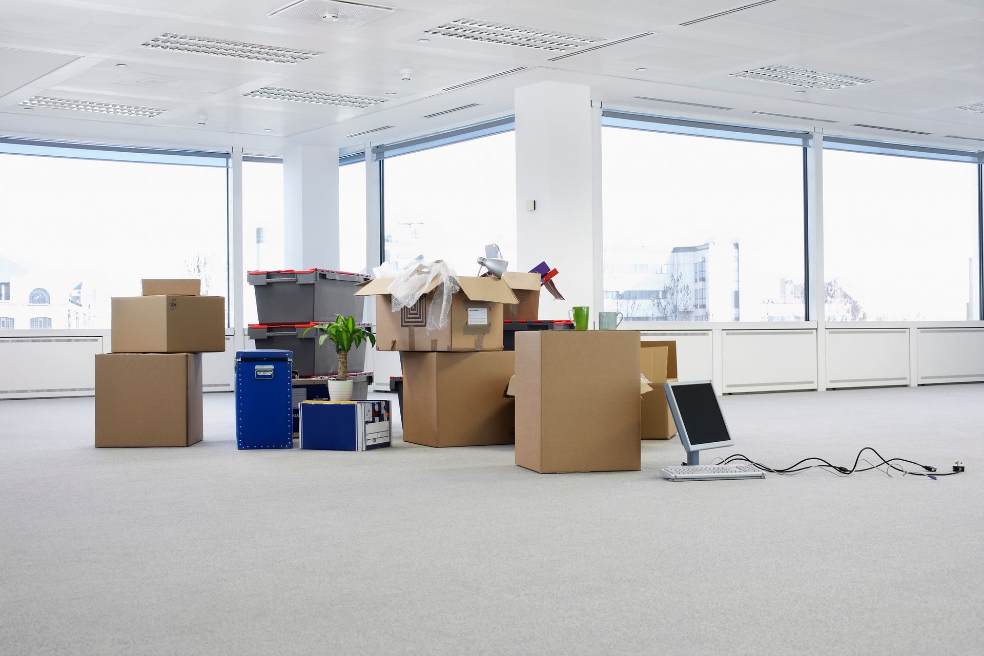 Boxes and items scattered in empty office space with large windows.