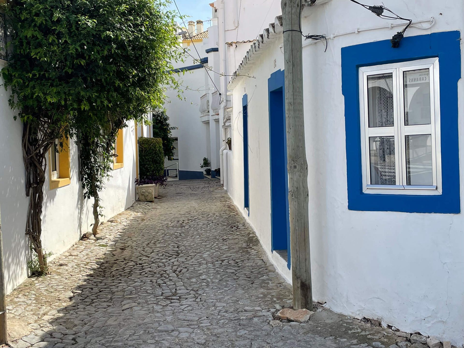 Eine schmale Gasse mit weißen Gebäuden und blauen Fenstern an der Algarve