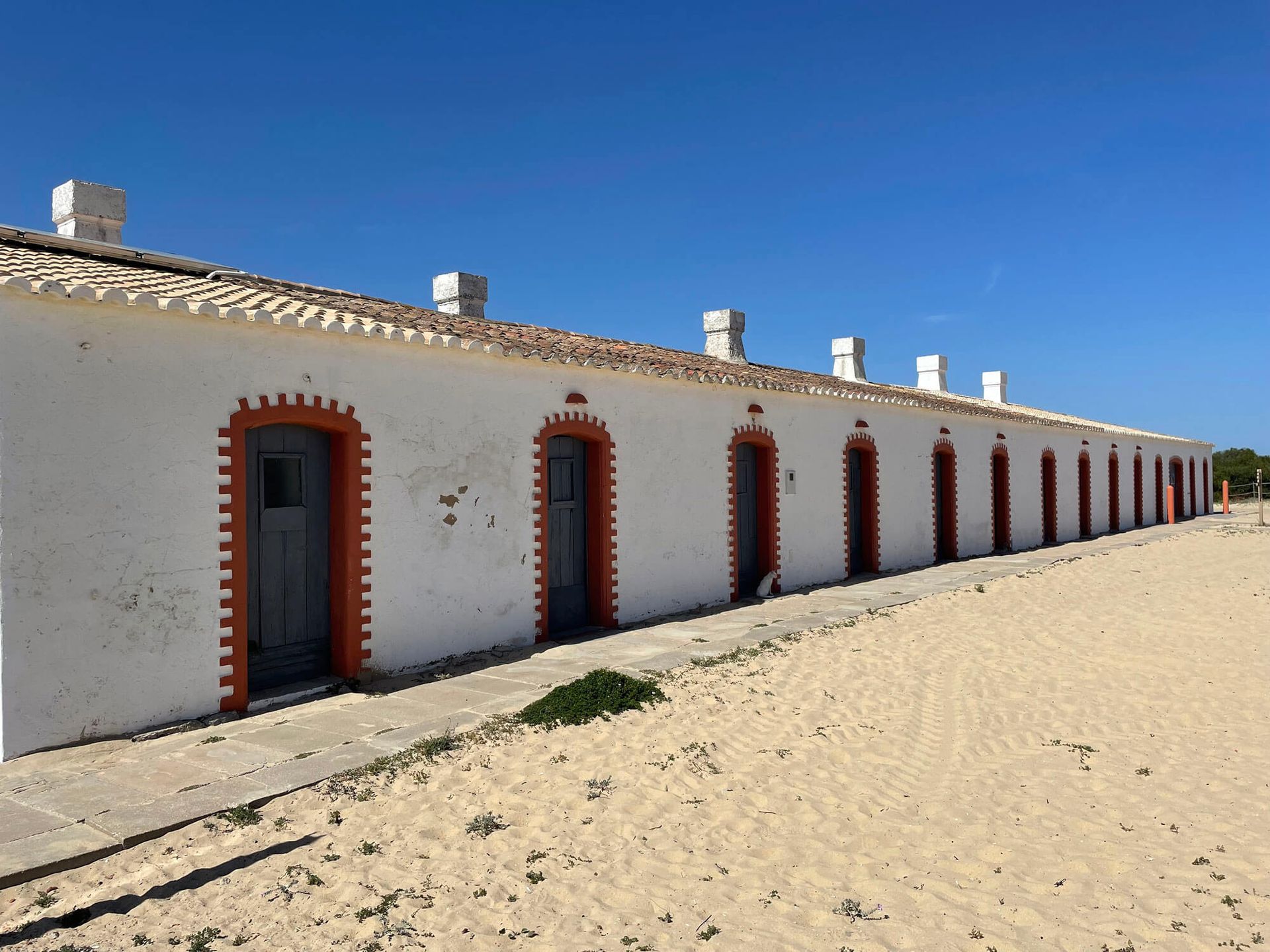 Algarve: weißes Gebäude mit roten Verzierungen an einem Sandstrand 