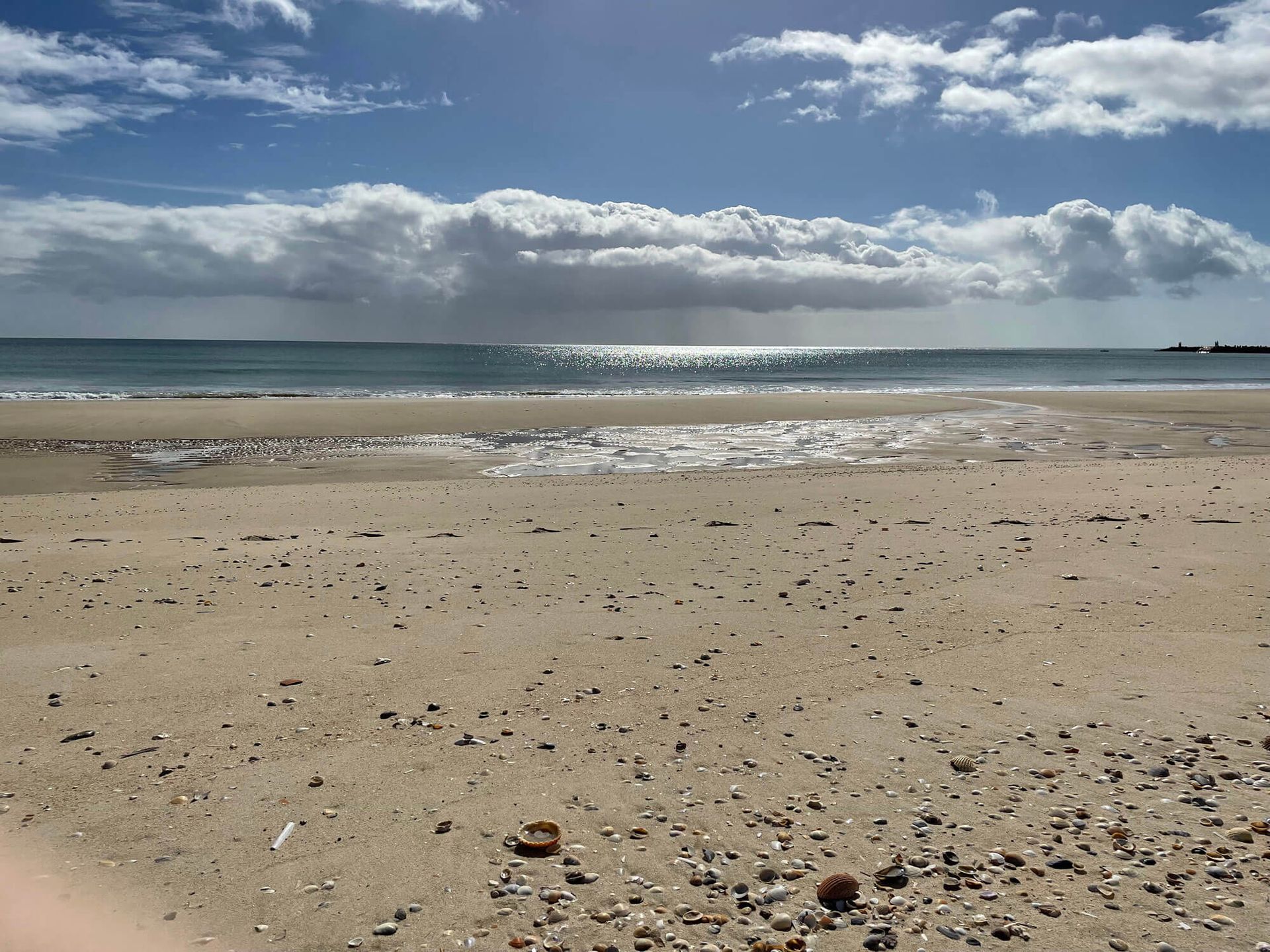Algarve: ein Sandstrand mit blauem Himmel und Wolken im Hintergrund