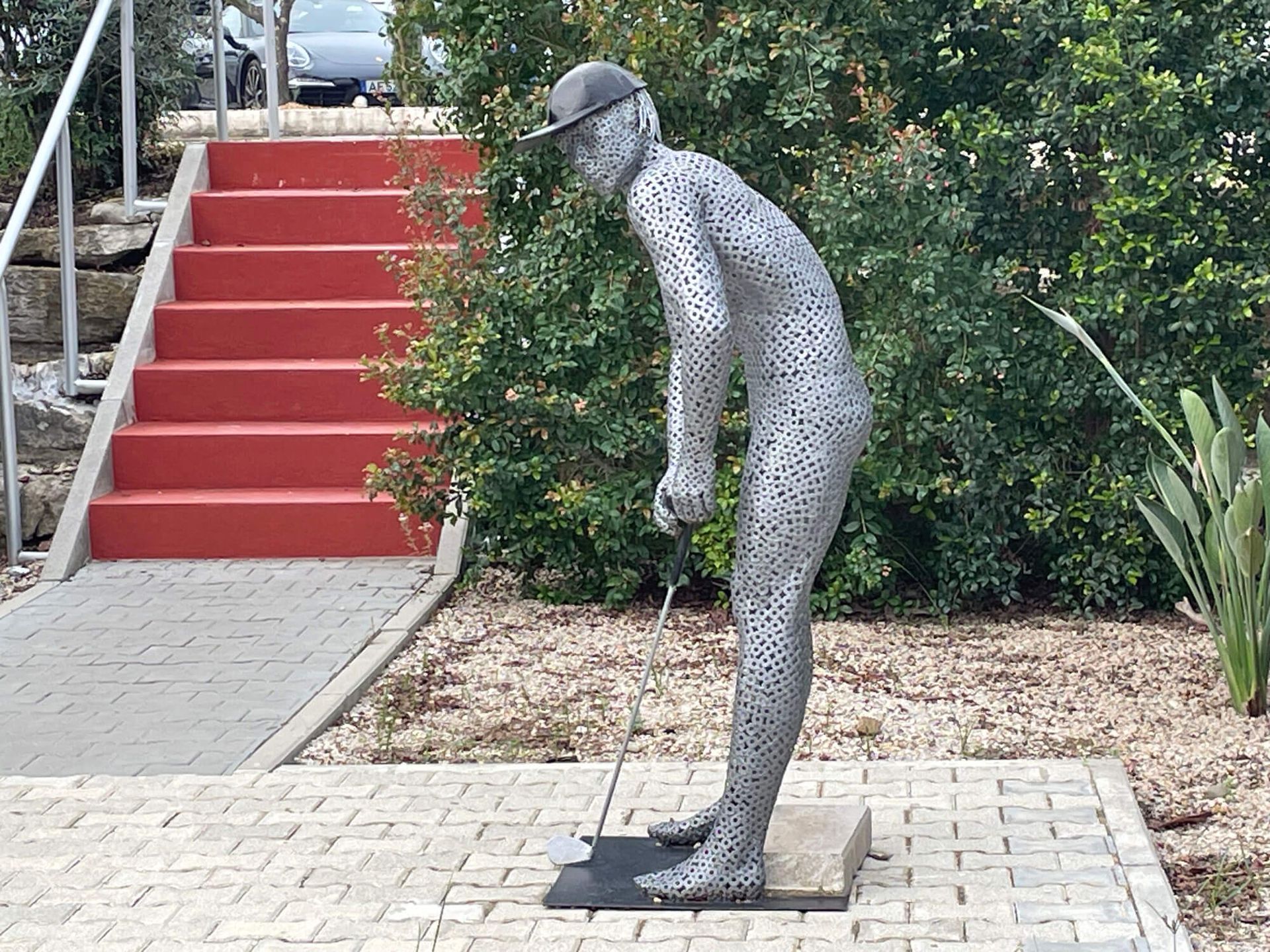 Algarve: Die Statue eines Golfers mit Baseballkappe steht vor einer roten Treppe.