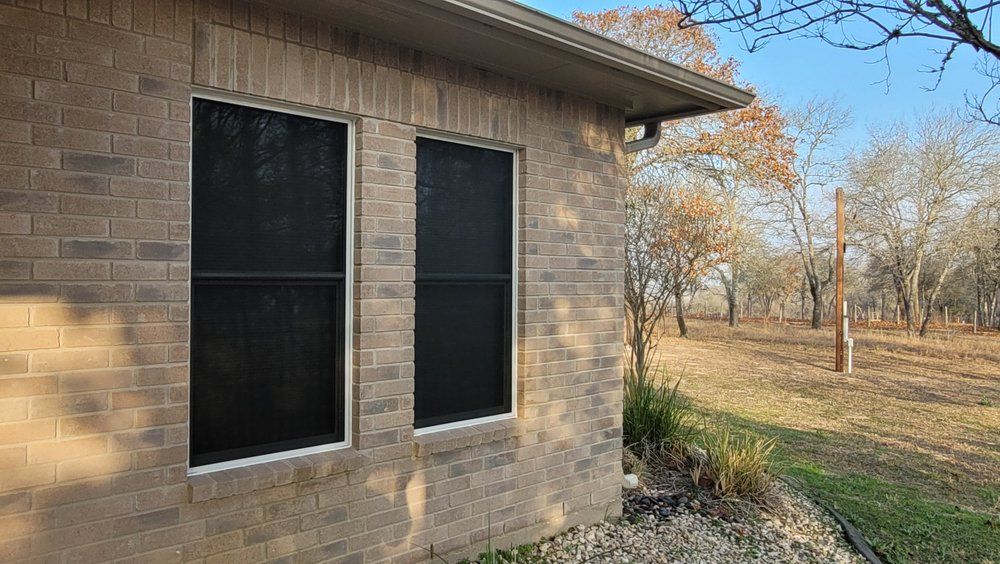 A brick house with two screened in windows on the side of it.