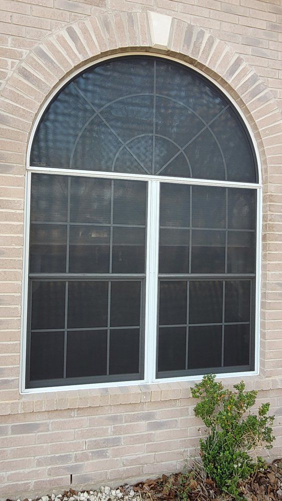 A window with a screen on it is on a brick wall.