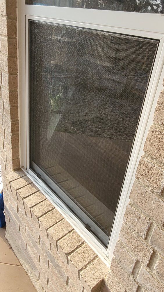 A white window with a screen on a brick wall.