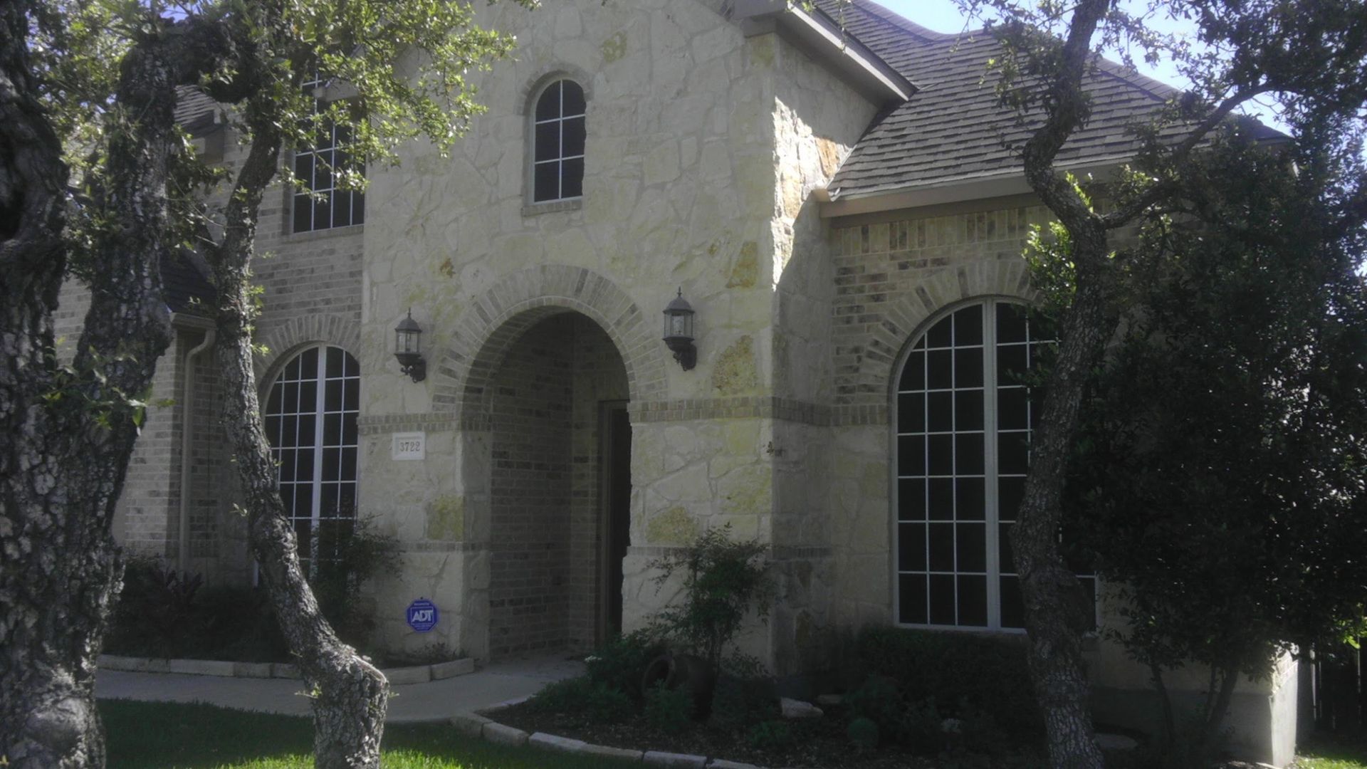 A large stone house with arched windows is surrounded by trees.