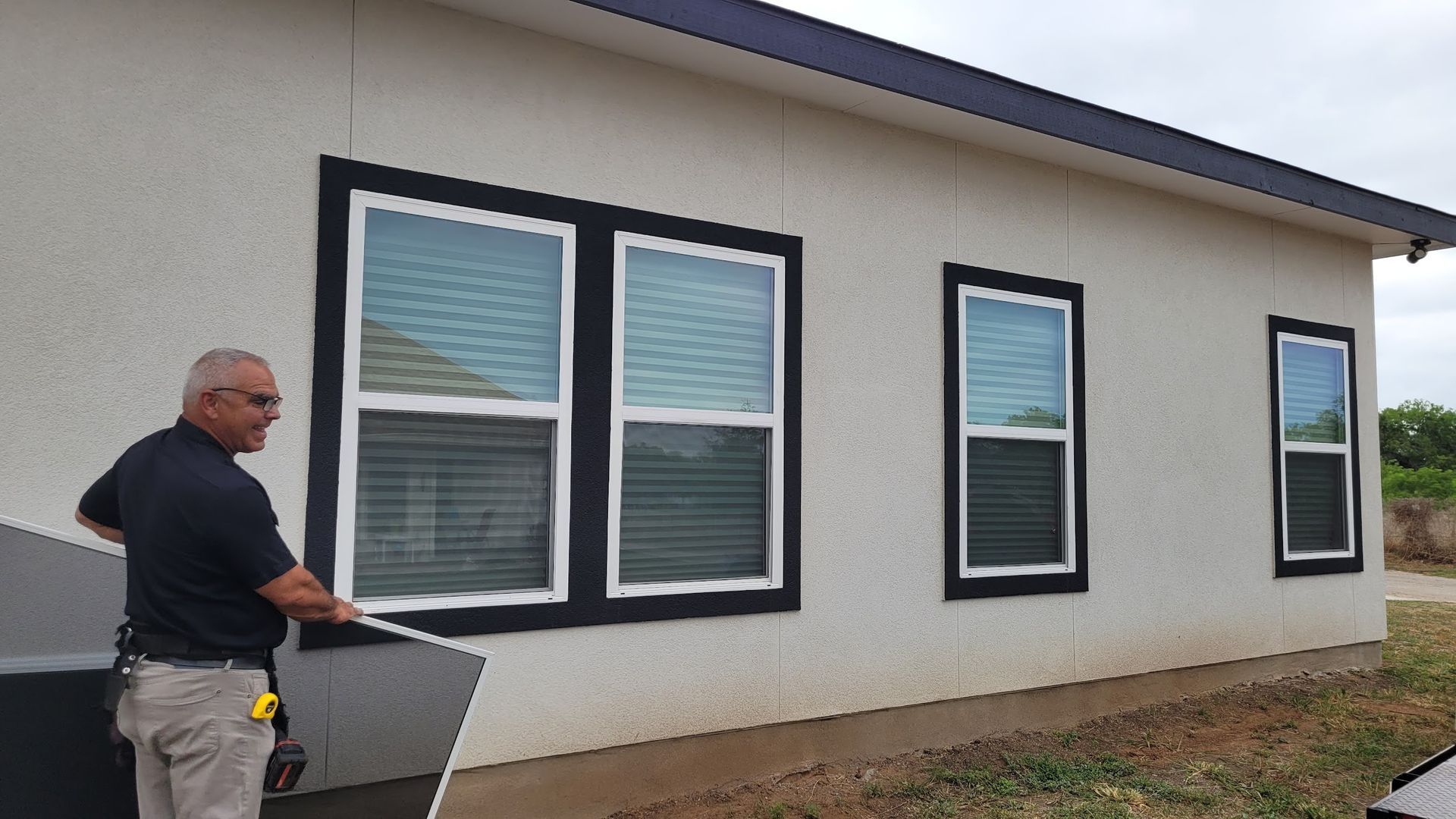 A man is measuring a window on the side of a house.