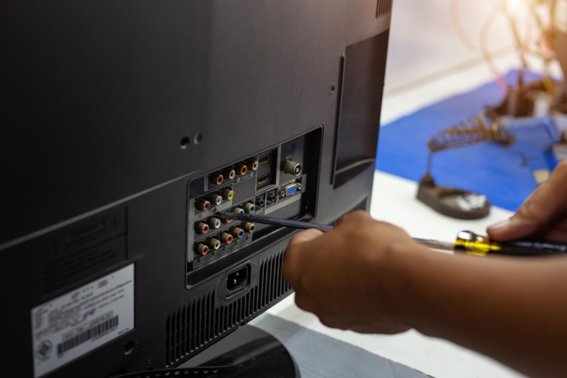 Hand plugging a cable into the back of a flat-screen TV with exposed ports