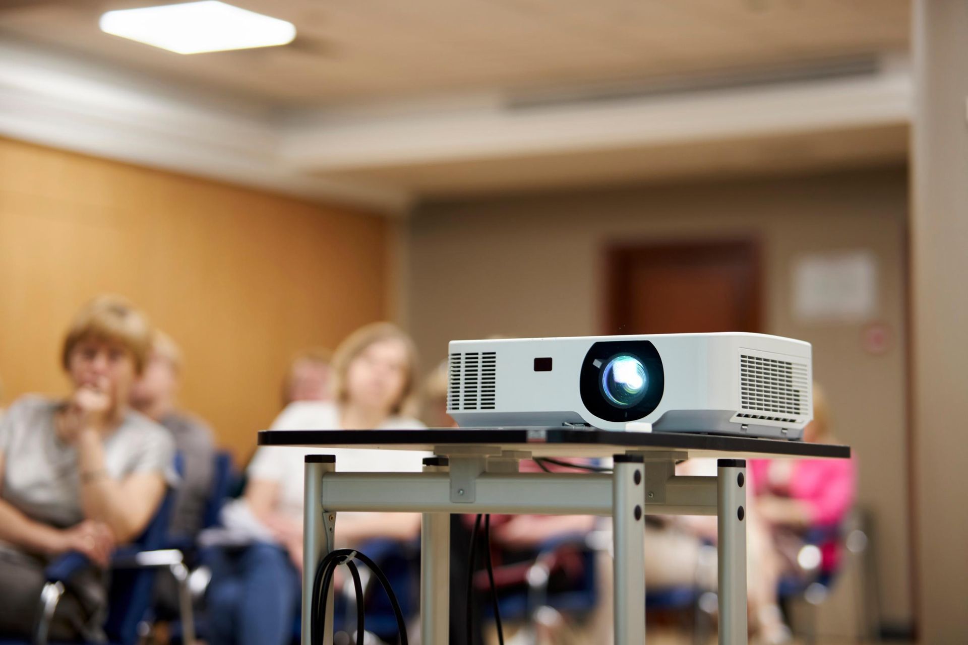 Projector on a cart in a classroom, with blurred students seated in the background.