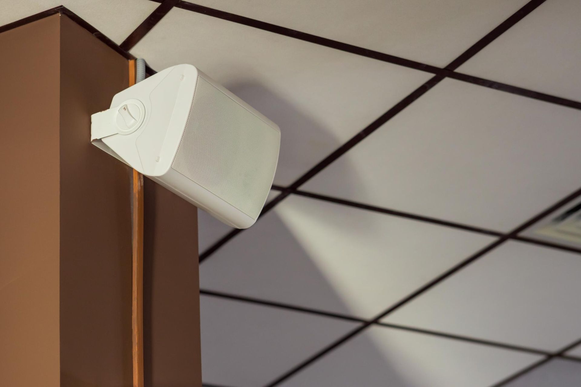 White wall-mounted speaker on a brown column beneath a tiled ceiling