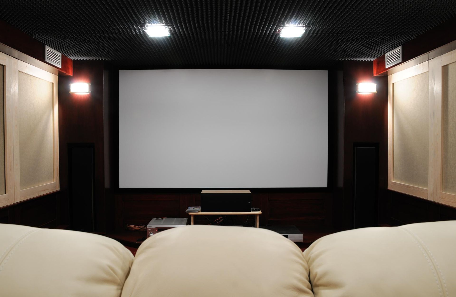 Home theater with large projection screen, front speakers, and cream-colored reclining seats
