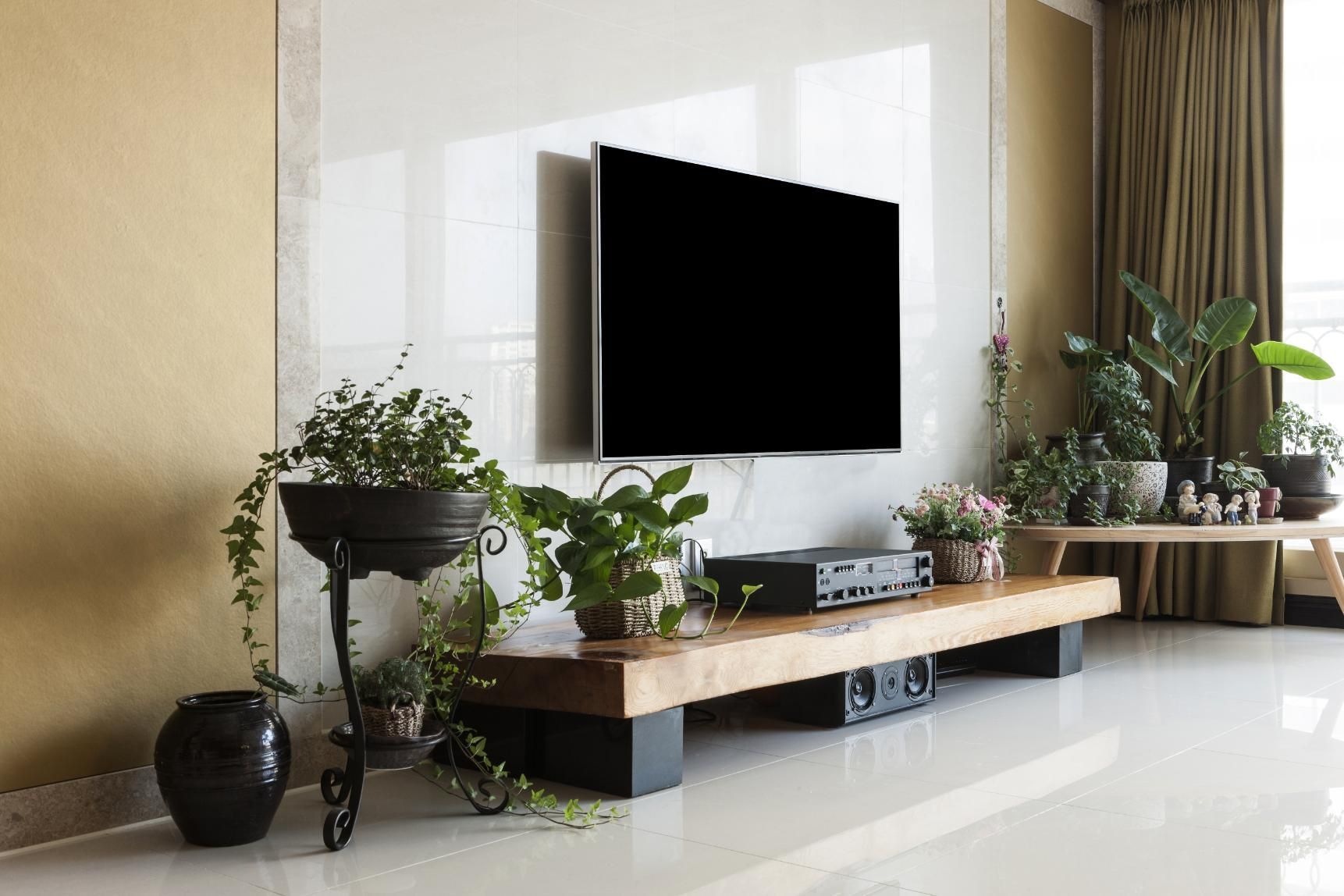 Modern living room with wall-mounted TV, wooden console, and potted plants on a glossy floor