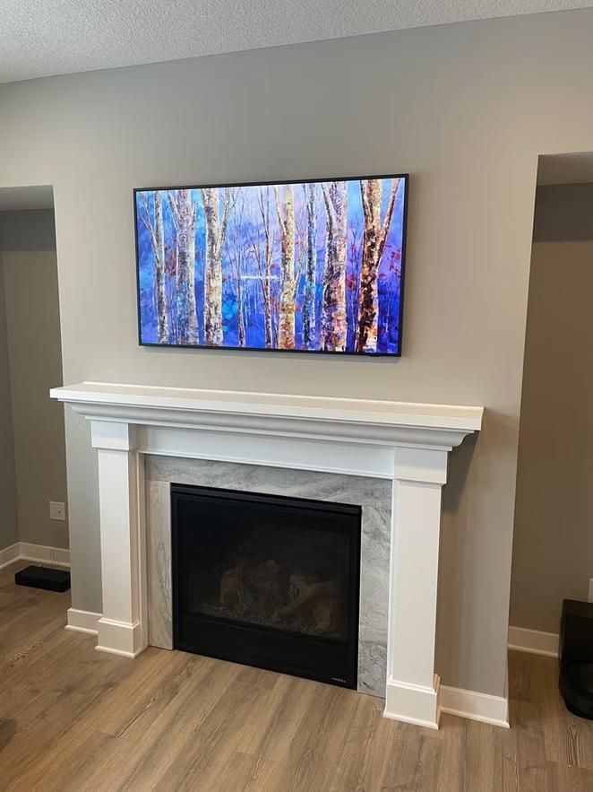 Modern living room fireplace with white mantel and wall-mounted TV showing a blue forest scene.
